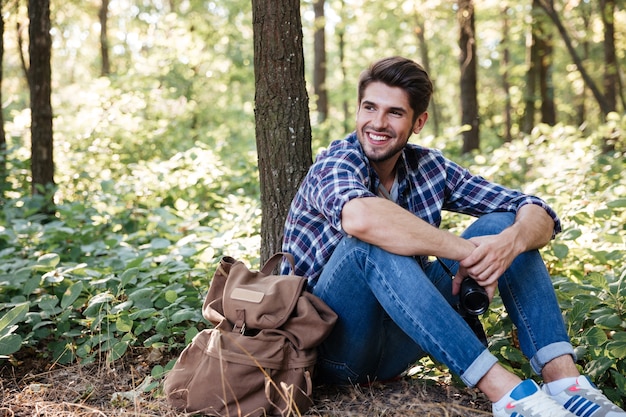 Homem sentado na floresta perto da mochila