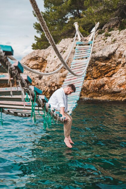 Homem sentado na ponte suspensa, apreciando a vista para o mar e a calma da natureza