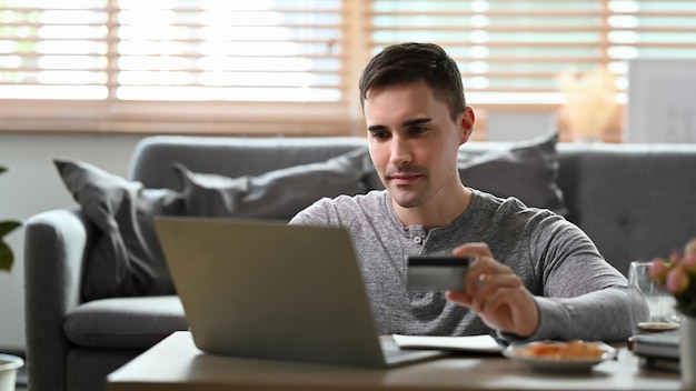 Homem sentado na sala de estar e fazendo transações bancárias on-line ou compras on-line com computador portátil