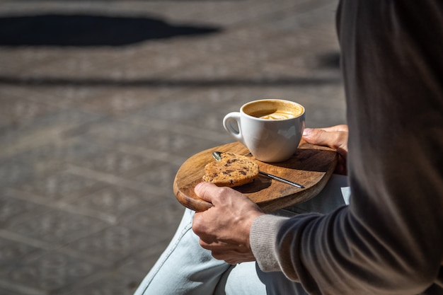 Homem sentado no café de rua com café e biscoito na bandeja de madeira