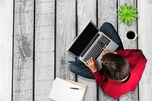 Homem sentado no chão de madeira usando laptop