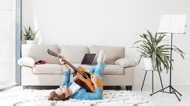 Homem sentado no chão e tocando guitarra vista longa