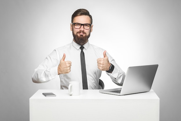 Homem sentado no escritório trabalhando em um laptop com um sorriso e mostrando o polegar