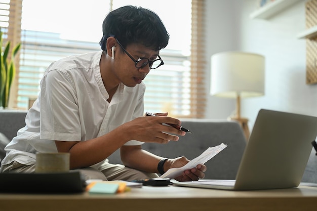 Homem sentado no sofá calculando despesas de despesas domésticas faz o pagamento no computador portátil