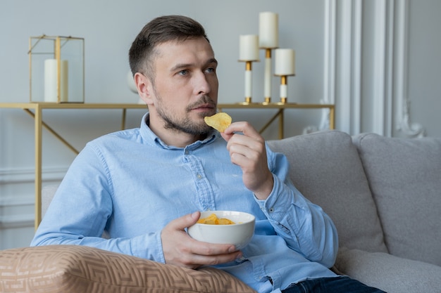 Homem sentado no sofá comendo batata frita