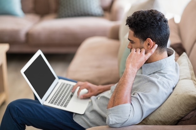 Homem sentado no sofá e usando o laptop na sala de estar