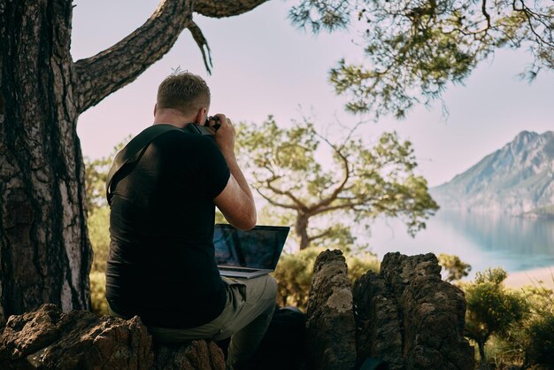 Homem sentado no topo da montanha e tirando fotos direto para o laptop Trabalhador remoto