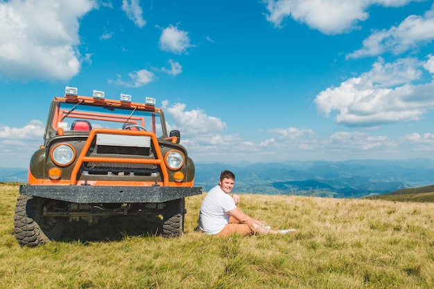 Foto homem sentado perto de um carro suv no topo da montanha com uma bela vista