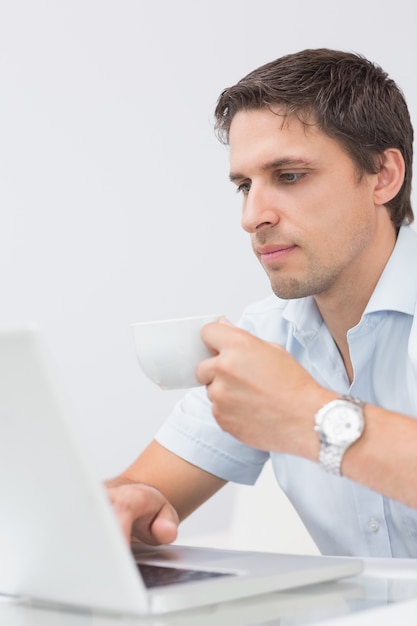 Homem serio com chávena usando laptop em casa