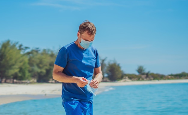 Homem sério e cansado decolar usando máscara de proteção médica azul Natureza mar areia praia floresta fundo do parque O sol brilha no rosto Pandemia Mundial de Coronavírus Parar a propagação do vírus