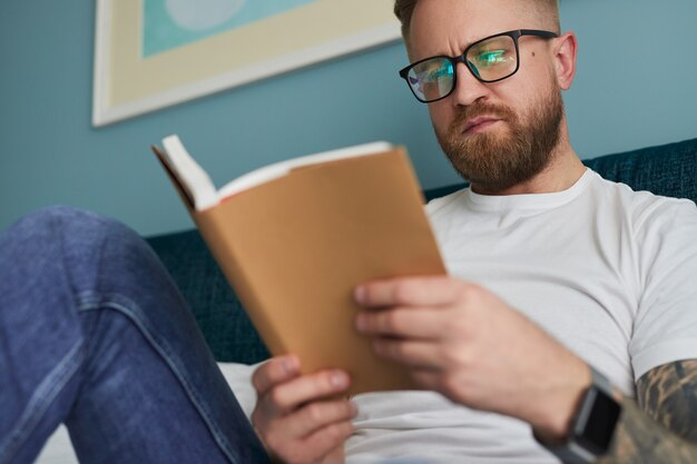 Homem sério lendo livro em casa