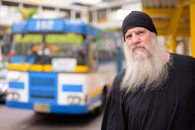 Homem sério maduro barbudo hippie esperando na parada de ônibus