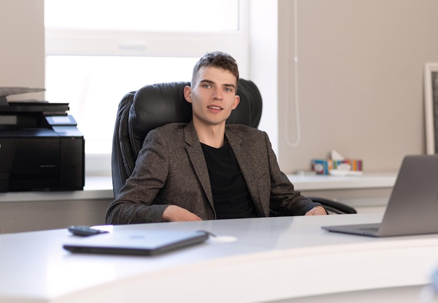 Homem sério sentado à mesa com documentos e laptop no escritório Coworking