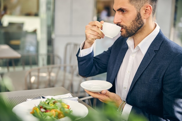 Homem sério tomando café, pensando profundamente enquanto espera por seu parceiro de negócios