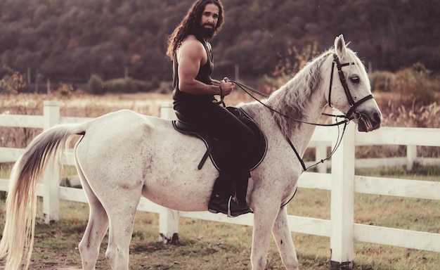 Homem sexy a cavalo Jovem jóquei treinando seu cavalo para um passeio O vaqueiro bonitão bonito anda a cavalo na bela natureza do campo