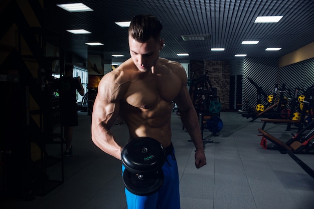 Homem sexy na academia com halteres. desportivo homem com grandes músculos