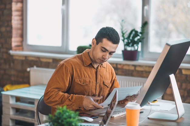 Foto homem simpático e sério olhando para o documento enquanto se concentra em seu projeto no trabalho