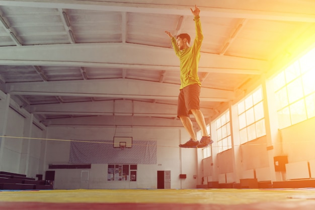 Homem slacklining andando e equilibrando em uma corda, slackline em um pavilhão desportivo