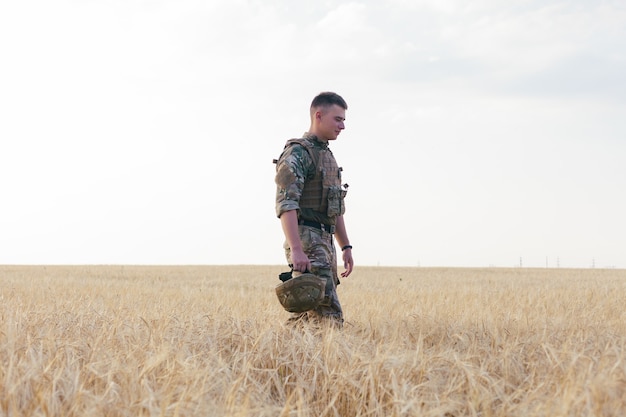 Homem soldado em pé contra um campo. Retrato de feliz soldado militar no campo de treinamento. Soldado do Exército dos EUA na Missão. guerra e conceito emocional.