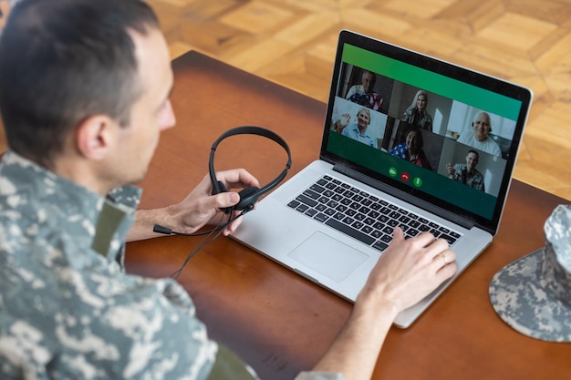 Homem soldado sorrindo enquanto faz uma chamada em conferência no laptop dentro de casa