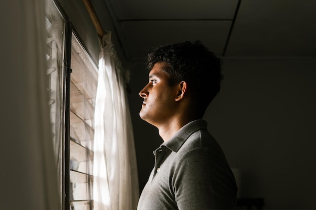 Foto homem solitário olhando e pensando na frente de uma janela conceito saúde mental e crise masculina