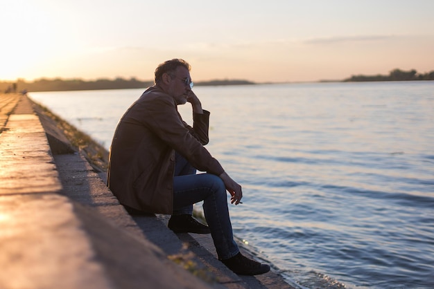 Homem solitário sentado nas escadas ao lado da margem do rio