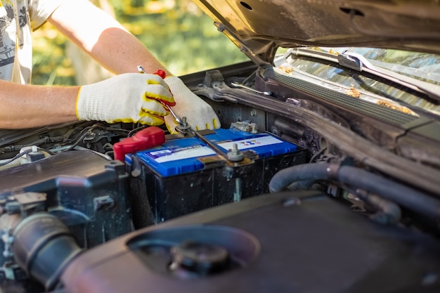 Foto homem solta os parafusos de montagem da bateria com uma chave inglesa, instalando e substituindo as peças sobressalentes em um carro.