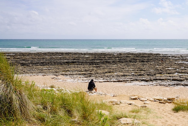 Homem solteiro sentado pedras na praia de areia atrás da vista traseira