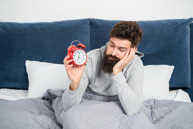 Homem sonolento olhando despertador na cama na hora da manhã