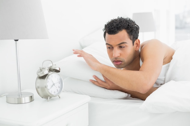 Homem sonolento olhando o despertador na cama