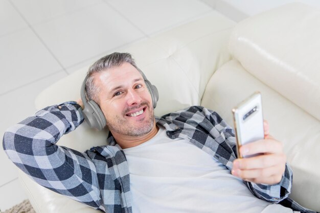 Homem sorridente a desfrutar de música com um telefone no sofá