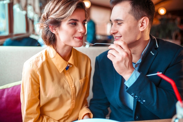 Homem sorridente alimentando mulher com colher em restaurante