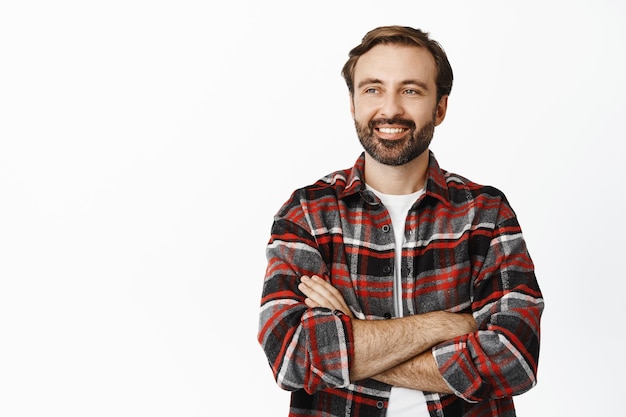 Foto homem sorridente bonito olhando feliz no espaço vazio para texto promocional cruzar os braços no peito sentindo-se satisfeito e relaxado fundo branco