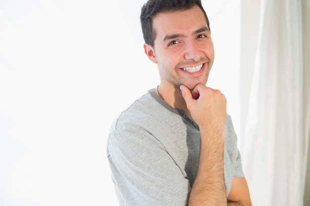 Homem sorridente casual olhando a câmera tocando queixo