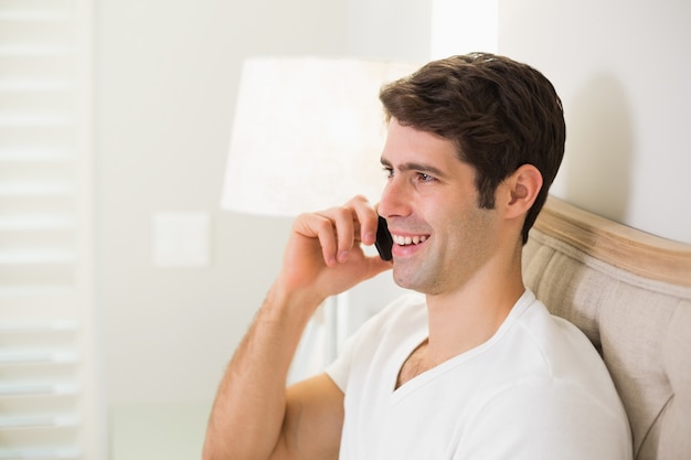 Homem sorridente casual usando celular na cama