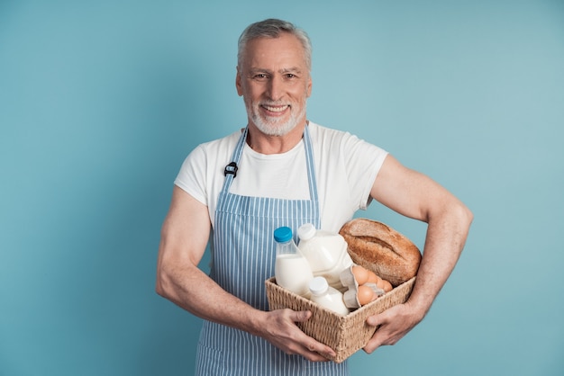 Homem sorridente com barba e cabelos grisalhos segurando uma cesta de comida