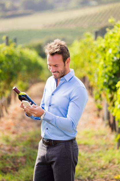 Homem sorridente com garrafa de vinho usando o telefone