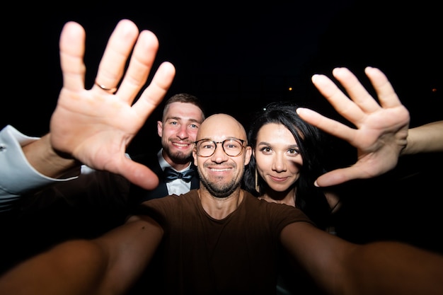 Homem sorridente com o casal de noivos tomando selfie à noite