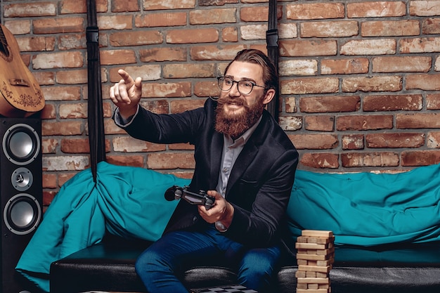homem sorridente com óculos, jogando um console de videogame e apontando o dedo para a frente.