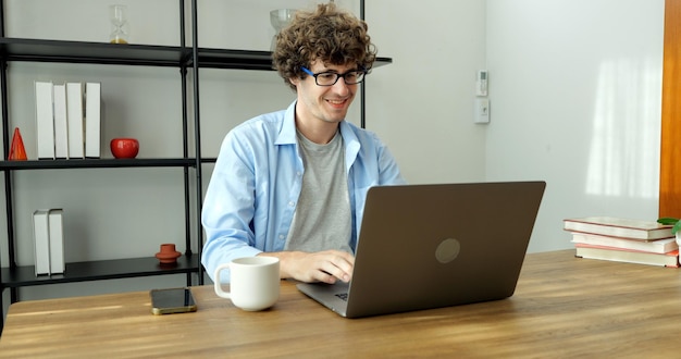 Homem sorridente com óculos usando laptop trabalhando em casa