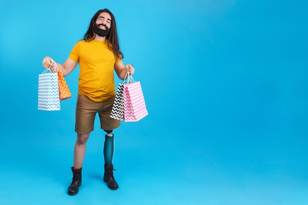 Homem sorridente com perna protética furando muitas sacolas de compras