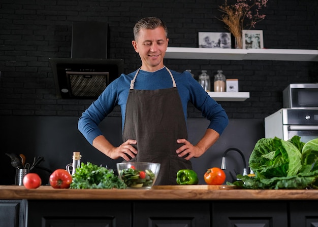 Homem sorridente cozinhando salada, cortando legumes frescos na cozinha preta moderna