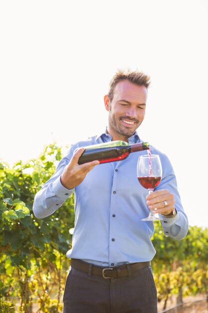 Foto homem sorridente, derramando vinho tinto de garrafa de vidro