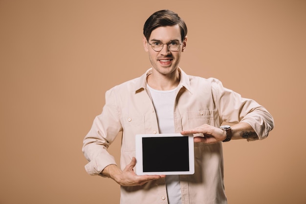 Homem sorridente em óculos segurando tablet digital com tela em branco isolada em bege