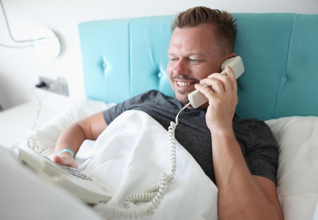 Foto homem sorridente encontra-se na cama e fala ao telefone