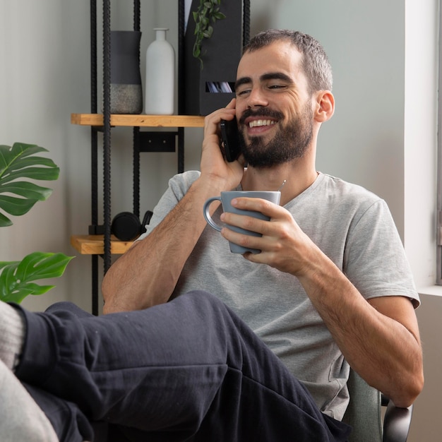 Foto homem sorridente falando ao telefone enquanto toma um café em casa