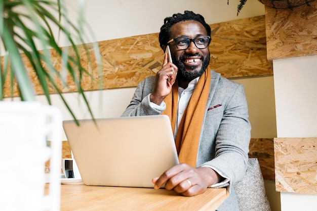 Homem sorridente falando no celular enquanto usa laptop em casa