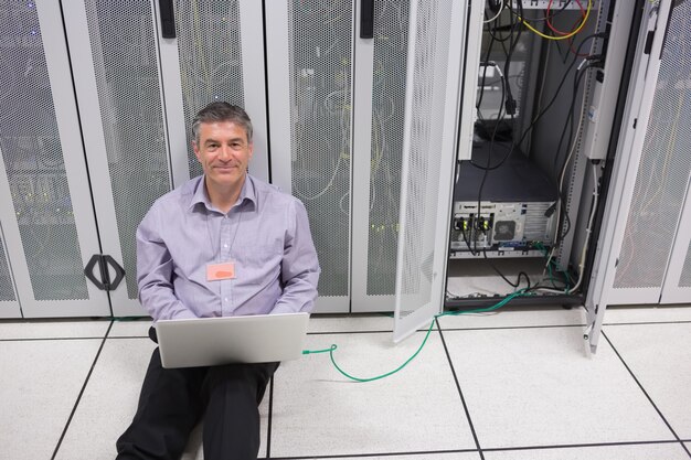 Homem sorridente fazendo manutenção de servidor com laptop