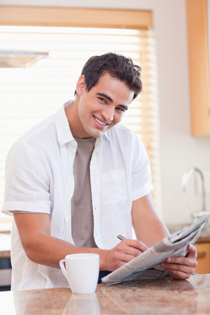 Homem sorridente fazendo palavras cruzadas na cozinha