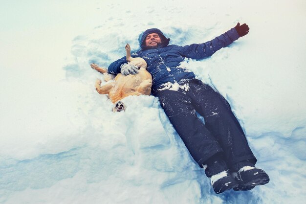 Homem sorridente feliz com cachorro labrador retriever deitado na neve